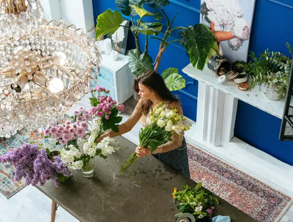 A floral designer arranging elegant purple and white blooms in a chic, modern studio with lush greenery.