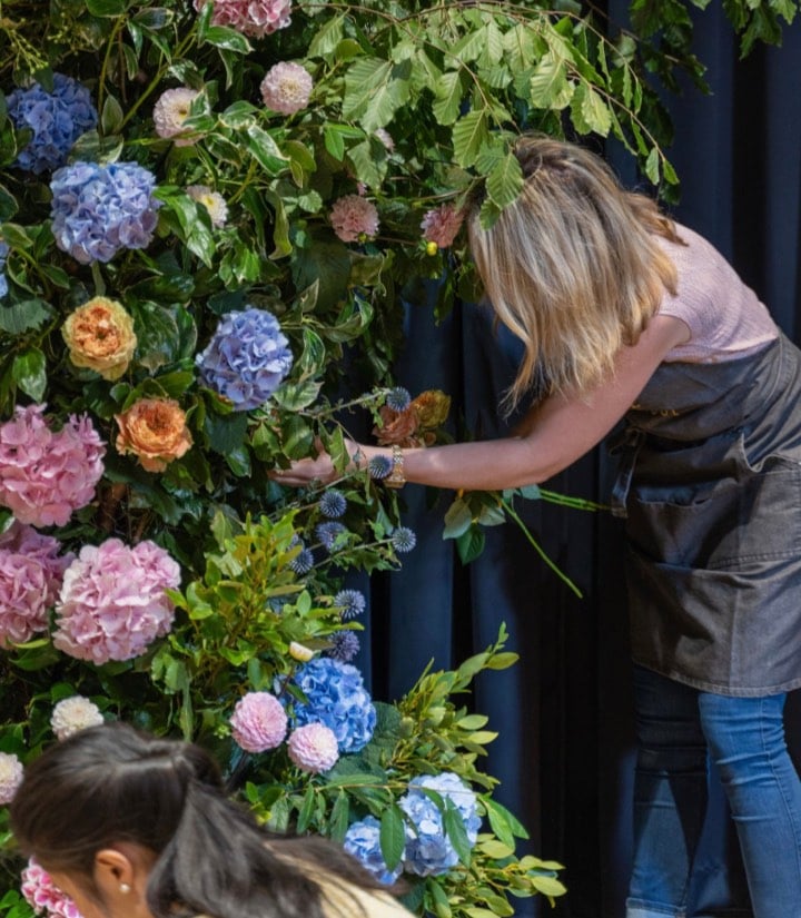 A floral arrangement featuring pink, blue, and orange hydrangeas with lush green foliage.