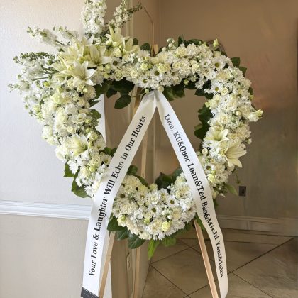 Endless Devotion Heart Wreath, an elegant floral design featuring white lilies and roses on a wooden easel stand.