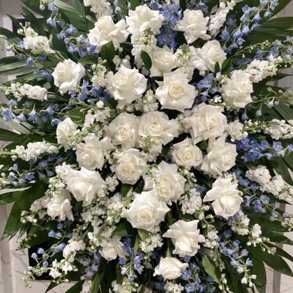 Gentle River Funeral Spray featuring white roses and blue delphinium in a serene floral arrangement.