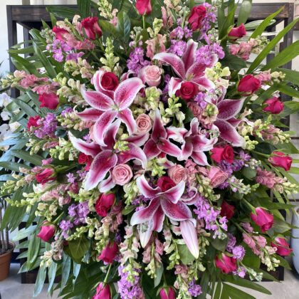 Tender Mercies Funeral Spray - Vibrant Floral Arrangement featuring pink lilies, roses, and lavender stock in a lush display.