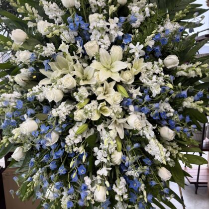 Ocean Breeze Funeral Spray - Elegant Floral Tribute featuring white roses, lilies, and blue delphinium in a lush arrangement.