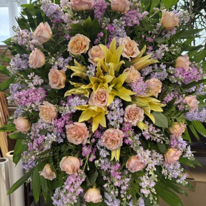 Noble Legacy Funeral Spray featuring soft peach roses and lavender stock flowers as an uplifting tribute.