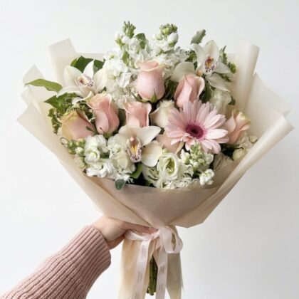Crema Di Pesca - Wrapped Bouquet featuring soft pink roses, white orchids, and delicate greenery, elegantly arranged.