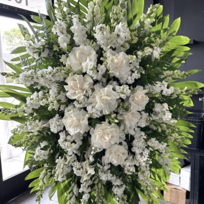 Winter Grace Funeral Spray - Comforting Elegance featuring white roses and stock flowers with lush green palm leaves.