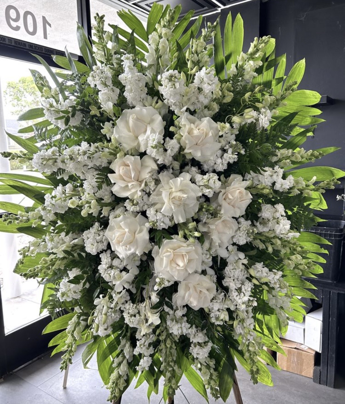 Winter Grace Funeral Spray - Comforting Elegance featuring white roses and stock flowers with lush green palm leaves.