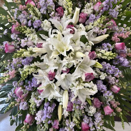 A luxurious floral arrangement featuring white lilies, pink roses, and lavender snapdragons, elegantly arranged.