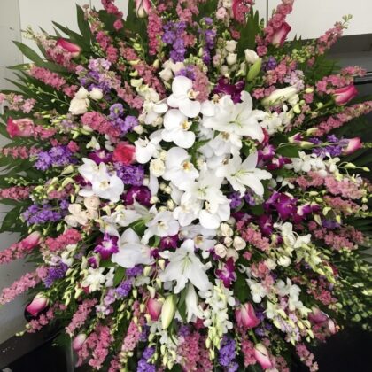 Vibrant Earthly Farewell Funeral Spray Arrangement featuring white lilies, orchids, and pink snapdragons in a lush display.