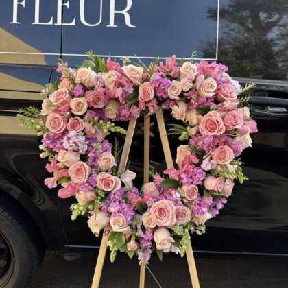 Serene Gardens Heart Wreath Tribute featuring blush roses and lavender stock flowers on a wooden easel.