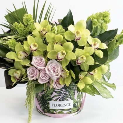 Luxurious arrangement featuring vibrant green orchids and soft lavender roses, elegantly styled in a chic floral bucket.