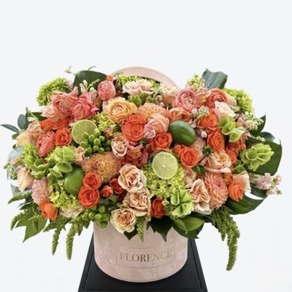 Luxurious floral arrangement featuring vibrant orange and soft pink roses, lush green accents, and lime slices.