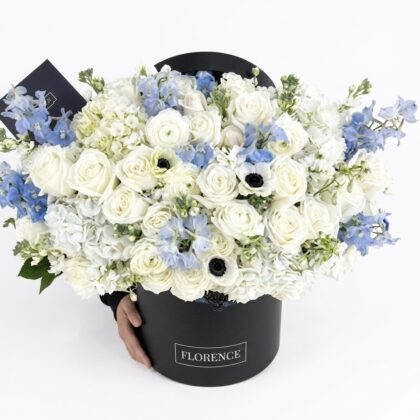 Luxurious arrangement of white roses and delicate blue delphiniums in an elegant black box.
