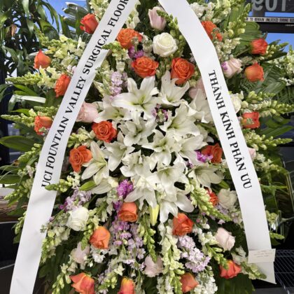 Heartfelt Autumn Peace Funeral Spray Tribute featuring vibrant orange roses, white lilies, and snapdragons in an elegant arrangement.