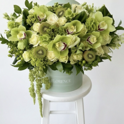 An elegant arrangement of white roses and green orchids, accented with kiwi slices and lush greenery.