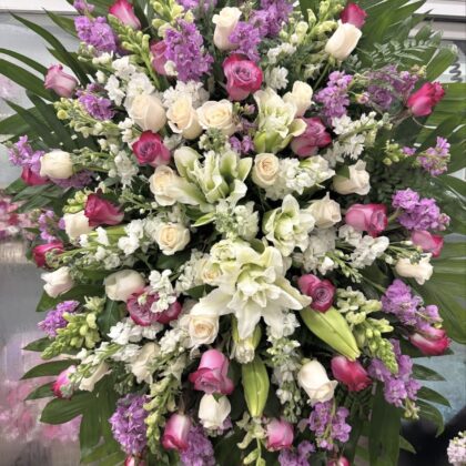 Elegant Whispering Pines Funeral Spray Tribute featuring white lilies, cream roses, and purple stock flowers.