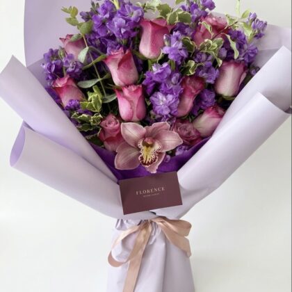 Midnight In Paris - Wrapped Bouquet featuring pink roses, purple delphiniums, and an elegant orchid, beautifully arranged.