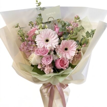 Primavera Bella - Wrapped Bouquet featuring soft pink roses, delicate gerberas, and lush greenery in an elegant arrangement.