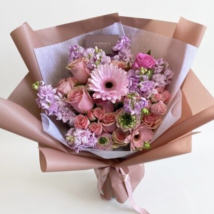 Acqua Di Rosa - Wrapped Bouquet featuring soft pink roses, delicate lilacs, and a vibrant pink gerbera daisy, elegantly arranged.