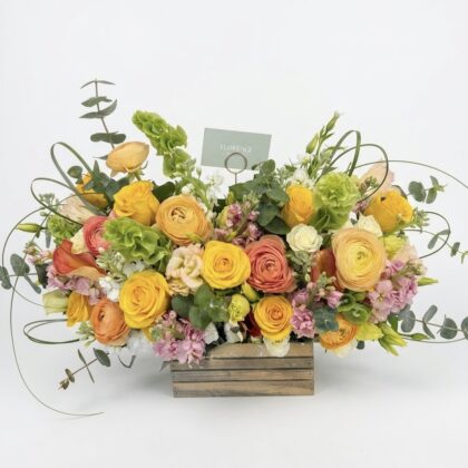 Sole E Sabbia - Wood Pot featuring vibrant ranunculus, roses, and lush greenery in a stunning arrangement.