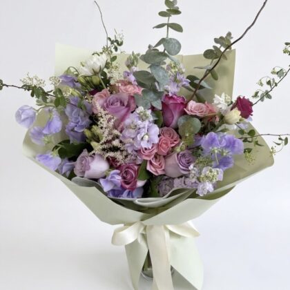 Elegant arrangement of soft pink and lavender roses, delicate blooms, and lush greenery in the Piccola Viola - Wrapped Vase.