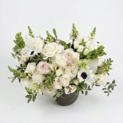 Luxurious floral arrangement featuring white roses, delicate ranunculus, and lush greenery in an elegant vase.