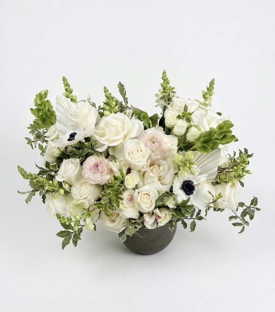 Luxurious floral arrangement featuring white roses, delicate ranunculus, and lush greenery in an elegant vase.