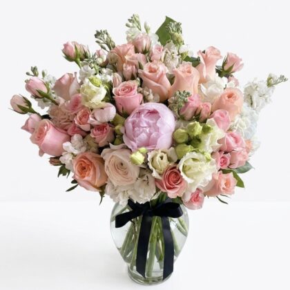 An elegant bouquet featuring soft pink roses, white peonies, and delicate greenery, arranged in a luxurious glass vase.