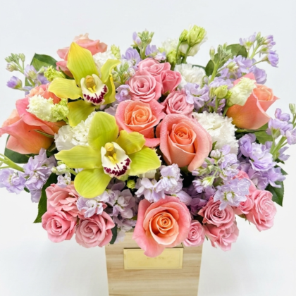 Luxurious arrangement featuring pink roses, green orchids, and delicate purple blooms in a chic wooden box.