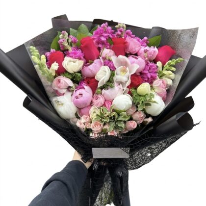 An elegant bouquet featuring vibrant pink roses, delicate peonies, and lush greenery, beautifully arranged.