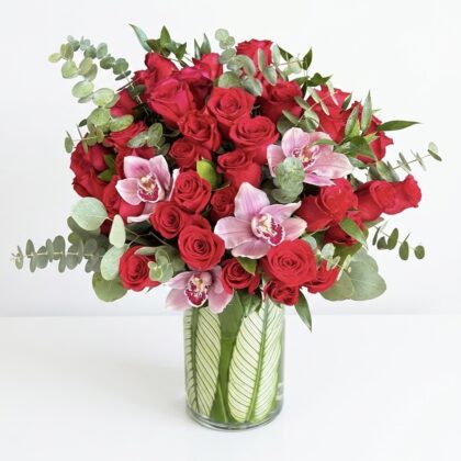 Luxurious arrangement of vibrant red roses and delicate pink orchids, accented with lush greenery.