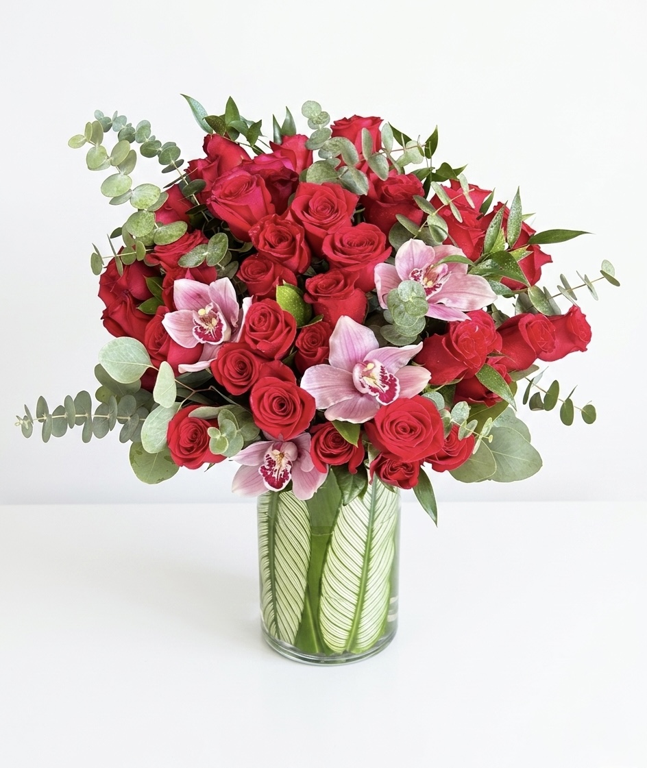 Luxurious arrangement of vibrant red roses and delicate pink orchids, accented with lush greenery.