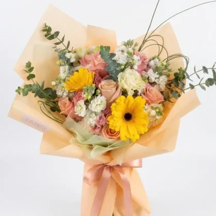 Sole E Fiore &ndash; Sunny Sophistication Bouquet featuring yellow gerberas, blush roses, and eucalyptus in peach wrapping.