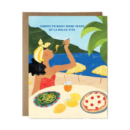 A woman in a red dress eats pasta by the sea on this elegant Cheers to La Dolce Vita Greeting Card.