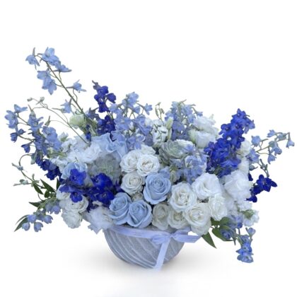 Cherie Bisou – Coastal Elegance Floral Vase featuring blue delphiniums, white roses, and succulents in a ceramic bowl.