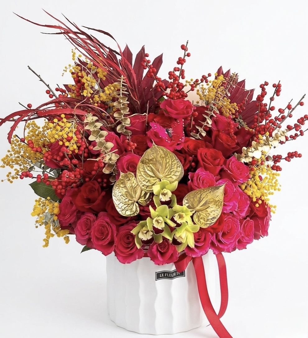 New Beginnings – Opulent Floral Design featuring red roses, gold anthuriums, and yellow mimosa in a white ceramic vase.
