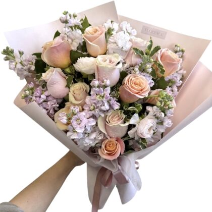A Delicate Cafe De Flore Wrapped Bouquet featuring soft peach roses and lavender stock flowers in elegant paper.