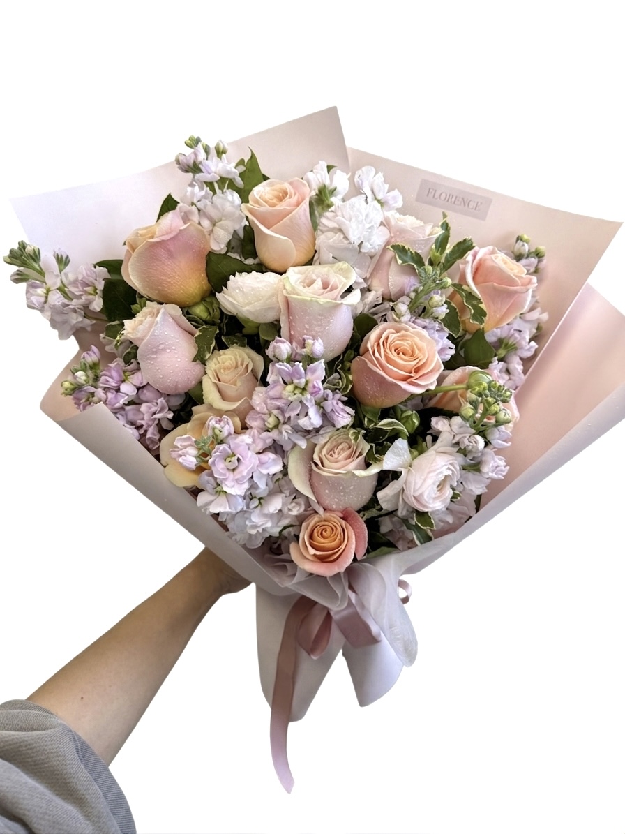 A Delicate Cafe De Flore Wrapped Bouquet featuring soft peach roses and lavender stock flowers in elegant paper.