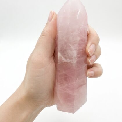 A hand holding a Stunning Rose Quartz Healing Tower for Home Decor against a clean white background.