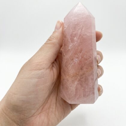 A hand holds a Lovely Rose Quartz Healing Tower for Positive Vibes against a clean, white background.