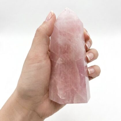 A hand holds an Exquisite Rose Quartz Healing Tower for Serenity, showcasing its pale pink, translucent crystalline texture.