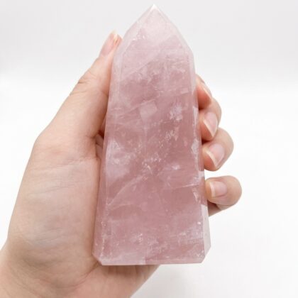 A hand holding a Unique Rose Quartz Healing Tower for Crystal Lovers, featuring a soft pink, translucent, faceted crystal.