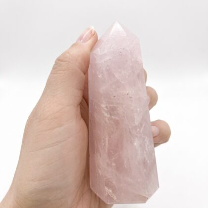 A hand holds a Gorgeous Rose Quartz Healing Tower for Wellness, featuring a soft pink hue and crystalline texture.