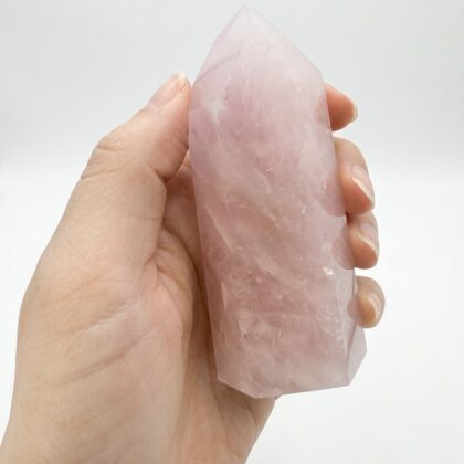 A hand holding a Stunning Rose Quartz Healing Tower for Home Decor with soft pink hues against a white background.