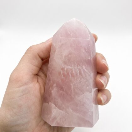 A hand holds a Rose Quartz 15 &ndash; Beautiful Crystal Tower, showcasing its soft pink hue and polished, faceted surface.