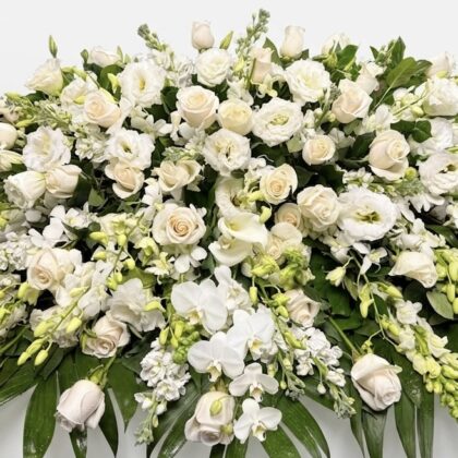 Villa Blanca Lush Casket Spray with White Roses featuring elegant orchids and greenery in a premium floral arrangement.