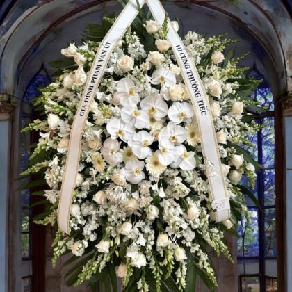 An Elegant White Cathedral Funeral Spray for Memorials featuring orchids, roses, and lush greenery in a grand arrangement.