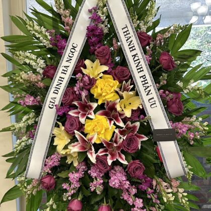 Infinite Grace – Vibrant Funeral Spray featuring deep purple roses, yellow roses, and lilies with lush green foliage.