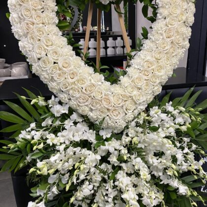 Forever Yours – Heart Wreath Double Layer Spray featuring pristine white roses and cascading orchids on a wooden stand.