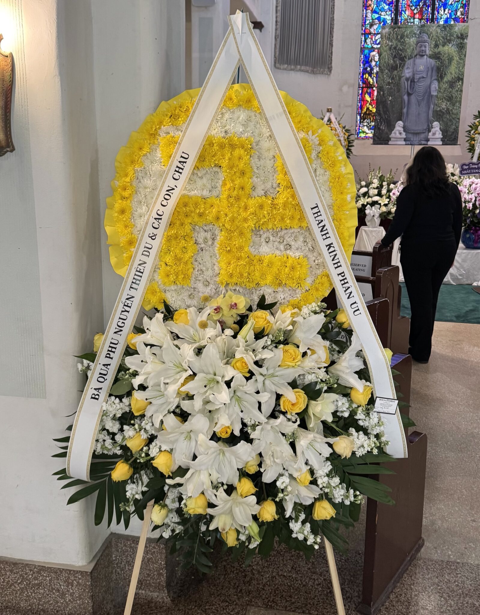 Peaceful Buddhist Symbol – Double Layer Spray featuring yellow and white chrysanthemums, lilies, and roses on a stand.