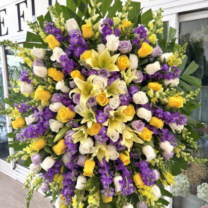 Tender Touch Funeral Spray - Vibrant Floral Arrangement featuring yellow lilies, purple stock, and white and yellow roses.
